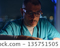 Medical worker wearing scrubs and glasses deeply concentrating at night 135751505