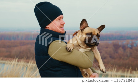Man Holding French Bulldog in Outdoor Landscape with Scenic View of Nature in the Background During a Beautiful Daylight Setting Man Holding French Bulldog in Outdoor Landscape with Scenic View of Nature in the Background During a Beautiful Daylight Setting 135751848
