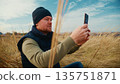 A Man Sitting in a Field Captures Nature's Beauty on His Smartphone, Embracing the Serenity of the Great Outdoors as He Enjoys a Peaceful Moment Surrounded by Tall Grass and a Clear Sky 135751871