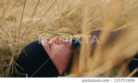 A Tranquil Moment of Solitude: A Man Resting in a Golden Field Surrounded by Tall Grass, Capturing Peaceful Connection with Nature and the Beauty of the Outdoors A Tranquil Moment of Solitude: A Man Resting in a Golden Field Surrounded by Tall Grass, Capturing Peaceful Connection with Nature and the Beauty of the Outdoors 135751899