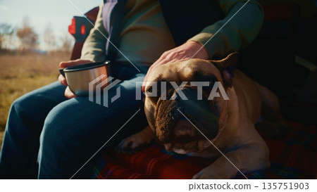 A Serene Moment: A Person Enjoys a Warm Beverage While Relaxing with Their Adorable French Bulldog Amidst Nature's Beauty on a Peaceful Day 135751903