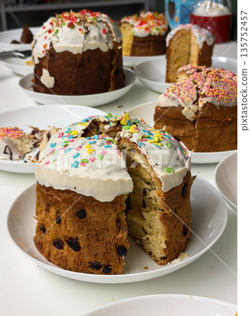 Traditional Easter cakes with white icing, colorful sprinkles, raisins are arranged on plates, sliced pieces reveal soft crumb, festive texture Traditional Easter cakes with white icing, colorful sprinkles, raisins are arranged on plates, sliced pieces reveal soft crumb, festive texture 135752457