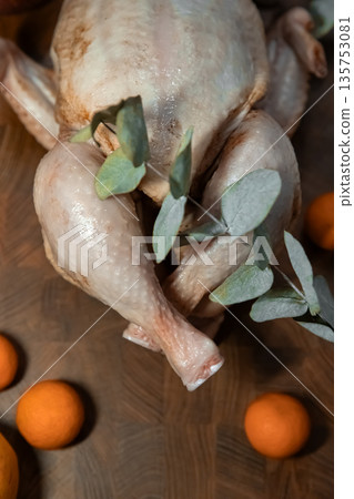 Raw chicken carcass on a wooden board with oranges and eucalyptus branch. Food preparation for Christmas or Thanksgiving dinner. Raw chicken carcass on a wooden board with oranges and eucalyptus branch. Food preparation for Christmas or Thanksgiving dinner. 135753081