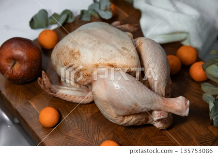 Raw whole chicken or turkey on a wooden cutting board with fruit and greens, concept for Thanksgiving and Christmas dinner preparation. 135753086