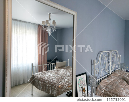 Reflection of a bedroom with bed and chandelier in a large mirror. Interior design for comfortable home living space. Reflection of a bedroom with bed and chandelier in a large mirror. Interior design for comfortable home living space. 135753091