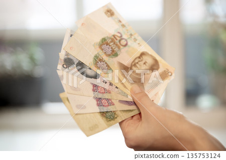 Woman hand holding Chinese yuan banknotes, showing money and financial concept. Currency exchange and personal finance theme. 135753124