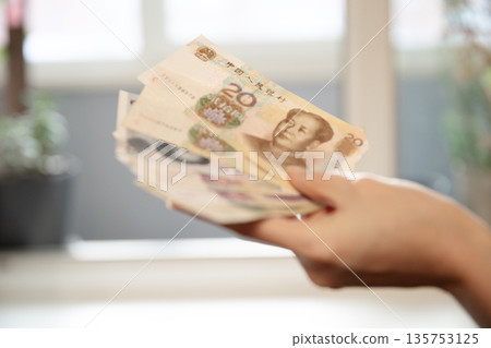 Woman holding a stack of twenty yuan banknotes. Chinese currency concept for finance, economy, wealth, and saving money. Woman holding a stack of twenty yuan banknotes. Chinese currency concept for finance, economy, wealth, and saving money. 135753125