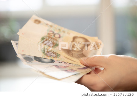Woman hand holding chinese yuan banknotes. Economic banking, finance exchange, or investment concept. Financial currency for global trade. 135753126