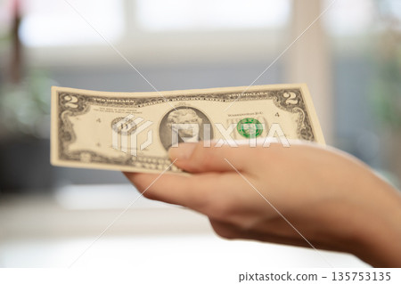 Woman holding a two dollar bill in her hand. Financial concept for money, transaction, payment, budget, income, or investment. Woman holding a two dollar bill in her hand. Financial concept for money, transaction, payment, budget, income, or investment. 135753135