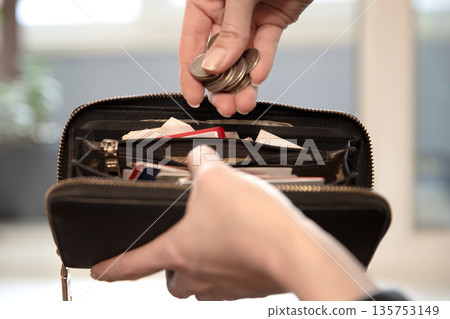 Woman putting coins into a black wallet. Financial literacy and money saving concept. Budgeting and managing personal finances. Woman putting coins into a black wallet. Financial literacy and money saving concept. Budgeting and managing personal finances. 135753149