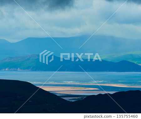 View of Castlemaine Harbour from a mountain vantage point on a cloudy day, showing distant hills and tidal flats. 135755460