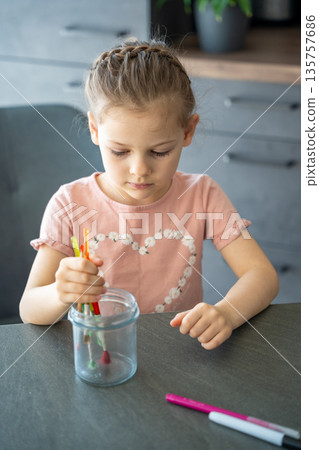 Child holding a glass jar and looking at it closely. Exploring shapes and transparency as part of craft activity. 135757686