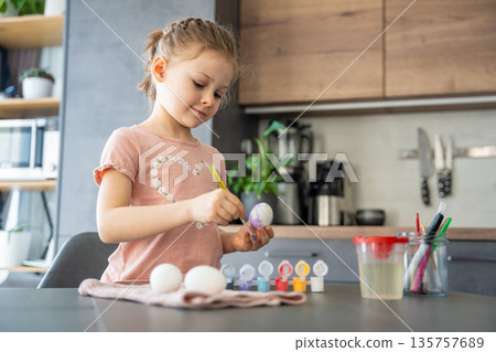 Child smiling while painting Easter eggs at the table. Joyful participation in seasonal family traditions. Child smiling while painting Easter eggs at the table. Joyful participation in seasonal family traditions. 135757689