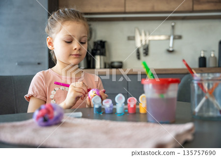 Girl dipping brush into purple paint before applying it on egg. A thoughtful step in creative tradition and learning process. Girl dipping brush into purple paint before applying it on egg. A thoughtful step in creative tradition and learning process. 135757690