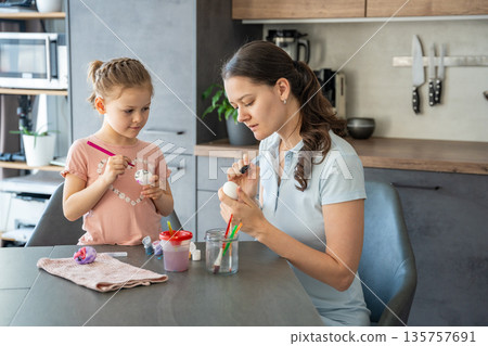 Child holding egg carefully while applying green paint with concentration. Hands-on learning and family tradition at home. Child holding egg carefully while applying green paint with concentration. Hands-on learning and family tradition at home. 135757691