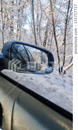 Car side mirror reflecting a snowy forest road during winter driving in daylight with frosty trees around. Image represents travel perspective, winter journey, movement and seasonal atmosphere Car side mirror reflecting a snowy forest road during winter driving in daylight with frosty trees around. Image represents travel perspective, winter journey, movement and seasonal atmosphere 135757727