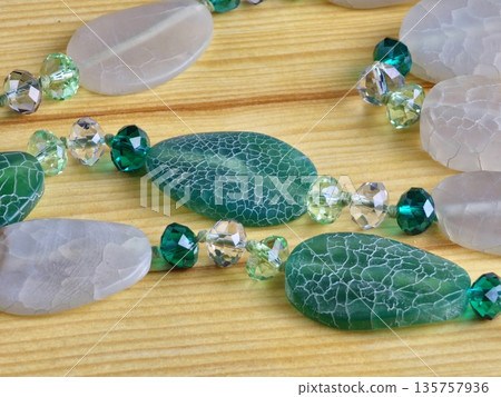 A close-up of handmade beads made of natural green and matte white agate with crackle effect on a wooden board A close-up of handmade beads made of natural green and matte white agate with crackle effect on a wooden board 135757936