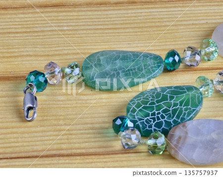 A close-up of handmade beads made of natural green and matte white agate with a crackle effect on wooden board A close-up of handmade beads made of natural green and matte white agate with a crackle effect on wooden board 135757937