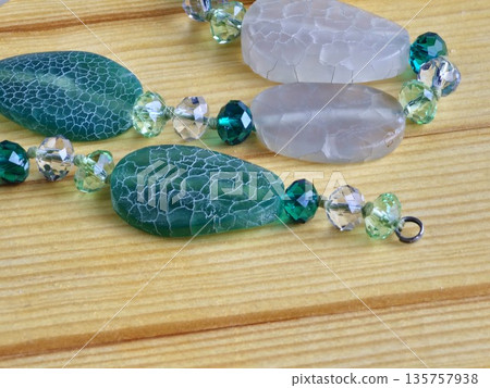 A close-up of handmade beads made of natural green and matte white agate with crackle effect on wooden board A close-up of handmade beads made of natural green and matte white agate with crackle effect on wooden board 135757938
