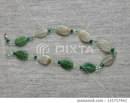 Handcrafted beads made of natural green and matte white agate with crackle effect on a burlap background Handcrafted beads made of natural green and matte white agate with crackle effect on a burlap background 135757942