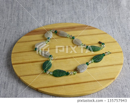 Handcrafted beads made of natural green and matte white agate with a crackle effect on a wooden board background Handcrafted beads made of natural green and matte white agate with a crackle effect on a wooden board background 135757943