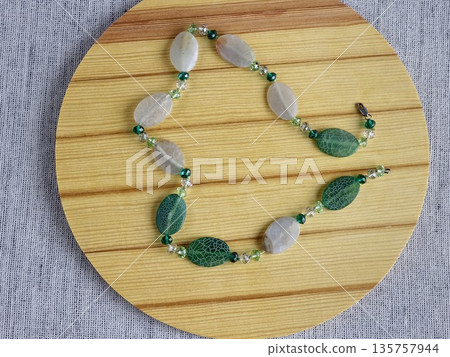 Handcrafted beads made of natural green and matte white agate with crackle effect on a wooden board background Handcrafted beads made of natural green and matte white agate with crackle effect on a wooden board background 135757944