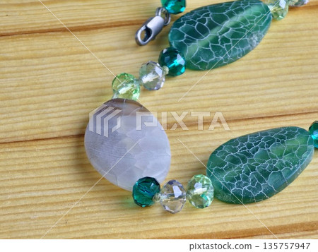 A close-up of handmade beads made of natural green and matte white agate with a crackle effect on a wooden board 135757947