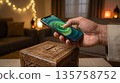 Hand Holding Smartphone for Online Zakat Donation in Cozy Home Setting with Blurred Lights 135758752