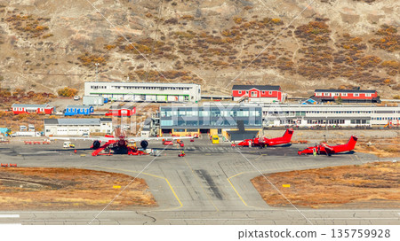 Red airplanes at airport runway and apron surrounded by tundra and mountains, showing arctic polar aviation operations and isolated transport hub in Kangerlussuaq, Greenland Red airplanes at airport runway and apron surrounded by tundra and mountains, showing arctic polar aviation operations and isolated transport hub in Kangerlussuaq, Greenland 135759928