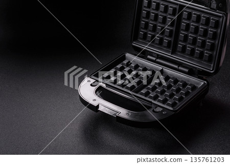A waffle iron, an electric machine for making Belgian breakfast desserts. A waffle iron A waffle iron, an electric machine for making Belgian breakfast desserts. A waffle iron 135761203