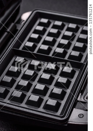 A waffle iron, an electric machine for making Belgian breakfast desserts. A waffle iron A waffle iron, an electric machine for making Belgian breakfast desserts. A waffle iron 135761214