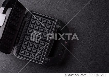 A waffle iron, an electric machine for making Belgian breakfast desserts. A waffle iron A waffle iron, an electric machine for making Belgian breakfast desserts. A waffle iron 135761216