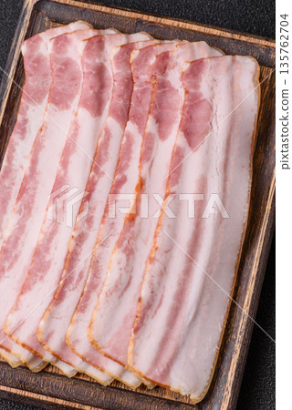 Raw smoked bacon slices, ham, jamon, or prosciutto strips for cooking. Raw bacon slices Raw smoked bacon slices, ham, jamon, or prosciutto strips for cooking. Raw bacon slices 135762704
