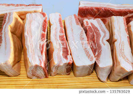 Bacon strips are placed neatly on wooden board for cooking meal preparation in kitchen setting. Bacon strips are placed neatly on wooden board for cooking meal preparation in kitchen setting. 135763029