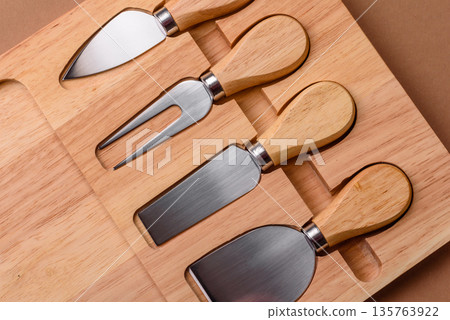 A set of cheese knives with a wooden cutting board, slicing tools. Cheese knives A set of cheese knives with a wooden cutting board, slicing tools. Cheese knives 135763922