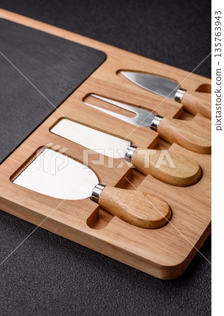 A set of cheese knives with a wooden cutting board, slicing tools. Cheese knives A set of cheese knives with a wooden cutting board, slicing tools. Cheese knives 135763943