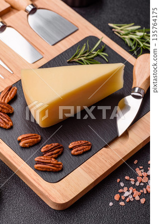 A wedge of cheddar, gouda, or parmesan cheese on a cutting board. Cheese wedge 135764175