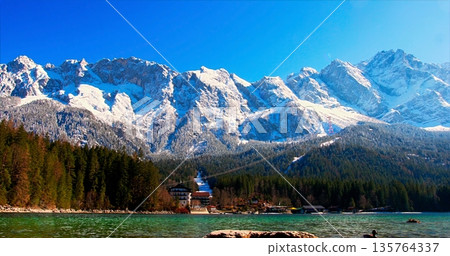 Tranquil Waters Near Snowy Peaks, Calm Turquoise Lake Beneath Snowcovered Mountains And Clear Blue Sky 135764337