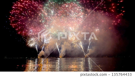 Reflective Fireworks Brighten Nighttime Scene, Colorful Explosions Illuminate Night Above Water Reflective Fireworks Brighten Nighttime Scene, Colorful Explosions Illuminate Night Above Water 135764433