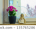 Cozy spring still life on a rainy window. Pink houseplant and textile toy creating home warmth on a cloudy day 135765286