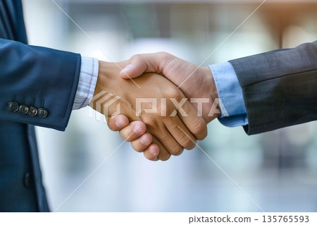 Hands of a businessman in a suit shaking hands in a business office to sign a contract Hands of a businessman in a suit shaking hands in a business office to sign a contract 135765593