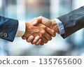 Hands of a businessman in a suit shaking hands in a business office to sign a contract 135765600