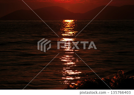 Vlora, Albania  August , 2025 A serene sunset over the Adriatic Sea, with warm golden light reflecting across gentle waves and distant silhouettes of mountains. The dramatic clouds and soft evenin 135766403
