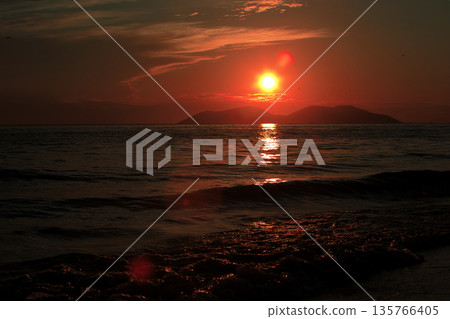 Vlora, Albania  August , 2025 A serene sunset over the Adriatic Sea, with warm golden light reflecting across gentle waves and distant silhouettes of mountains. The dramatic clouds and soft evenin 135766405