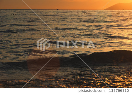 Vlora, Albania ,August , 2025 A serene sunset over the Adriatic Sea, with warm golden light reflecting across gentle waves and distant silhouettes of mountains. The dramatic clouds and soft evenin 135766510