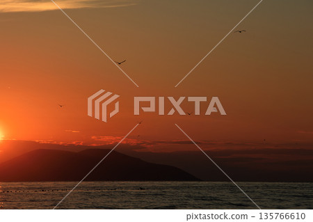 Vlora, Albania  August , 2025 A serene sunset over the Adriatic Sea, with warm golden light reflecting across gentle waves and distant silhouettes of mountains. The dramatic clouds and soft evenin 135766610