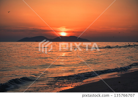 Vlora, Albania  August , 2025 A serene sunset over the Adriatic Sea, with warm golden light reflecting across gentle waves and distant silhouettes of mountains. The dramatic clouds and soft evenin 135766707