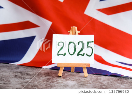Paper note with text 2025 on National symbol of Great Britain. British wave the UK silky flag background. Financial outlook planning, new year annual report Paper note with text 2025 on National symbol of Great Britain. British wave the UK silky flag background. Financial outlook planning, new year annual report 135766980