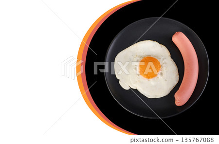 Fried egg and sausage on a black plate, on a black background, place under the text on a white background 135767088