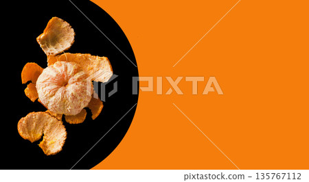 Peeled tangerine lies with peel on a black background, space for the text on an orange background Peeled tangerine lies with peel on a black background, space for the text on an orange background 135767112